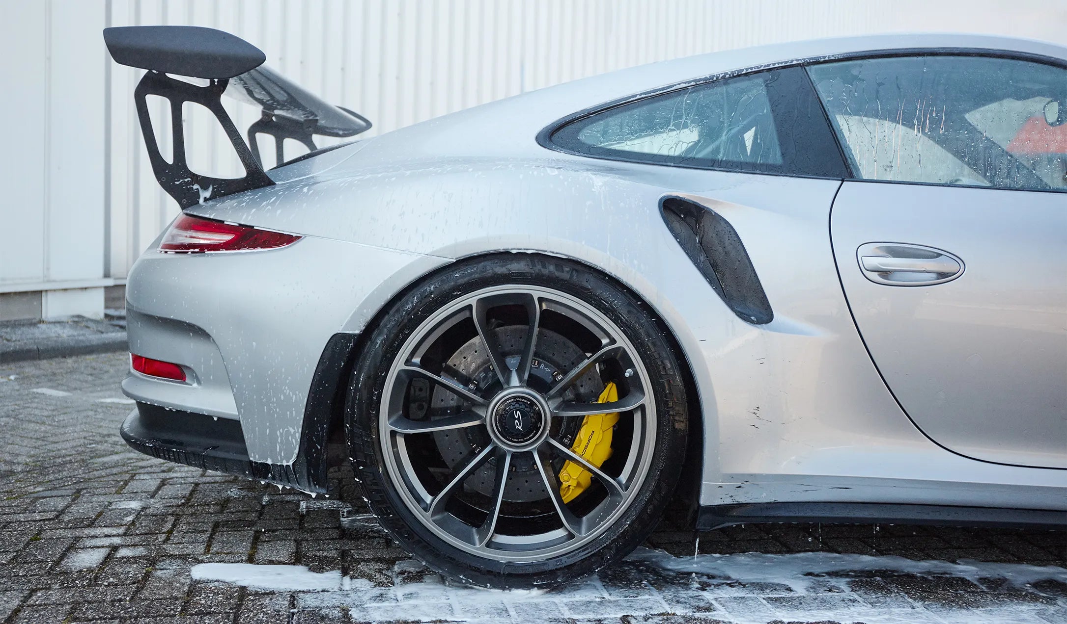 Fast Car Care auto shampoo en reiniging – schuimende zilveren Porsche sportwagen met gele remklauw – intensieve car detailing